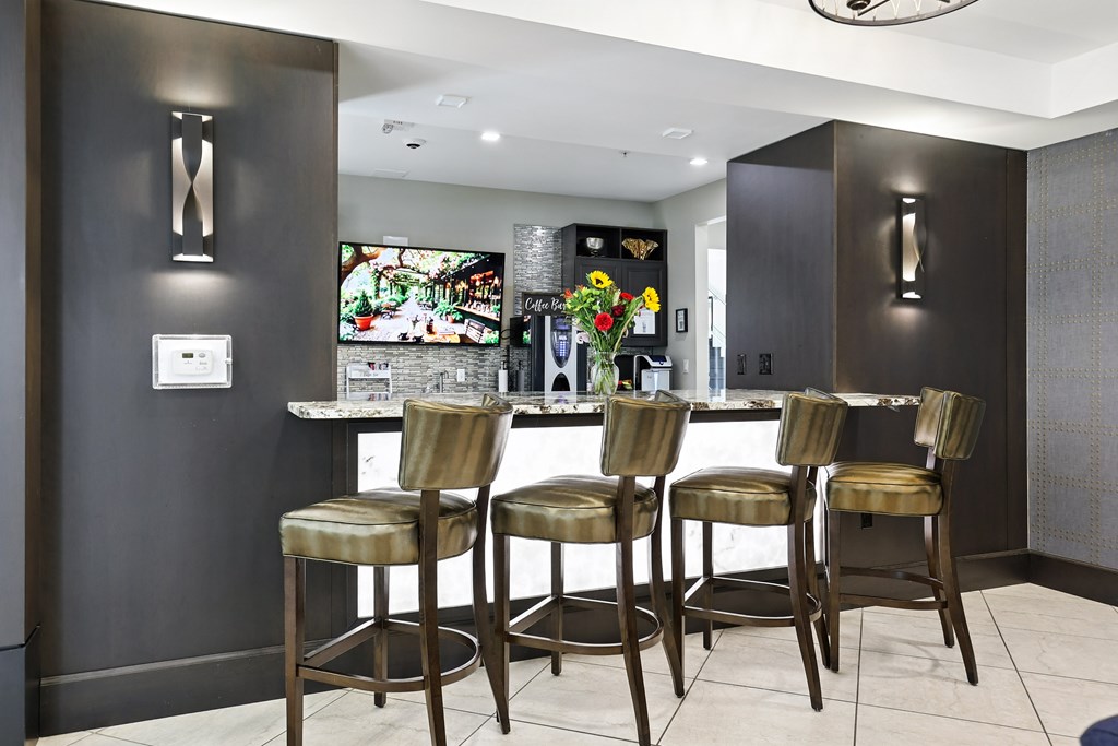 A bar area with three stools and a television in the background at Alinea Town and Country Luxury Apartments in Des Peres MO 63131.