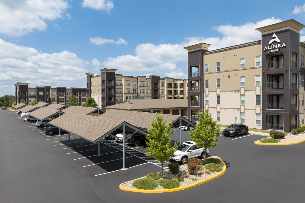 A parking lot in front of a building with the sign Alinea on it and carports at Alinea Town and Country Luxury Apartments in Des Peres MO 63131..