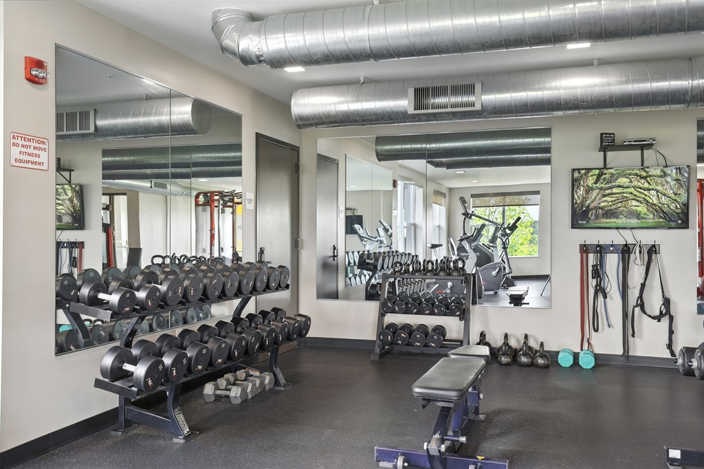 A gym with a variety of equipment including dumbbells, weight plates, and a bench press at Alinea Town and Country Luxury Apartments in Des Peres MO 63131.