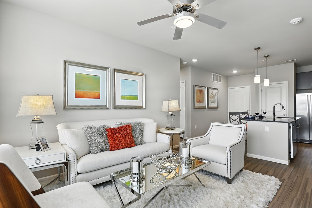 A modern living room with a white sofa, a glass coffee table, and a ceiling fan at Alinea Town and Country Luxury Apartments in Des Peres MO 63131.