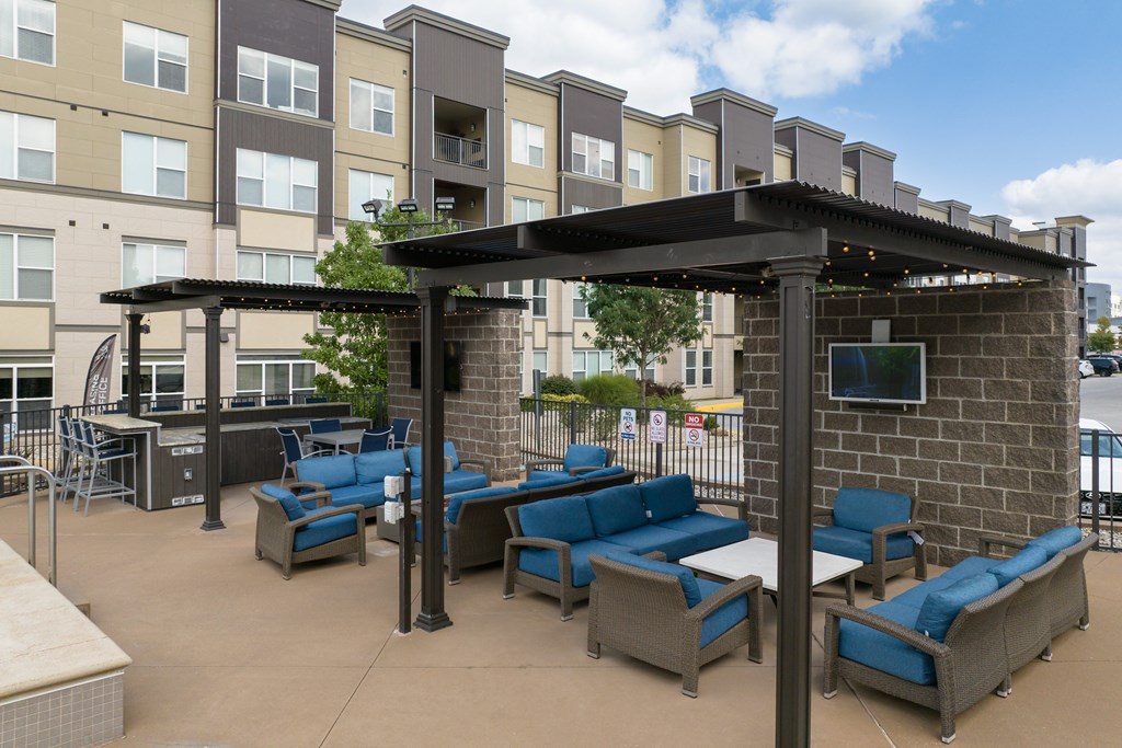A patio with blue cushioned furniture and a black pergola at Alinea Town and Country Luxury Apartments in Des Peres MO 63131..