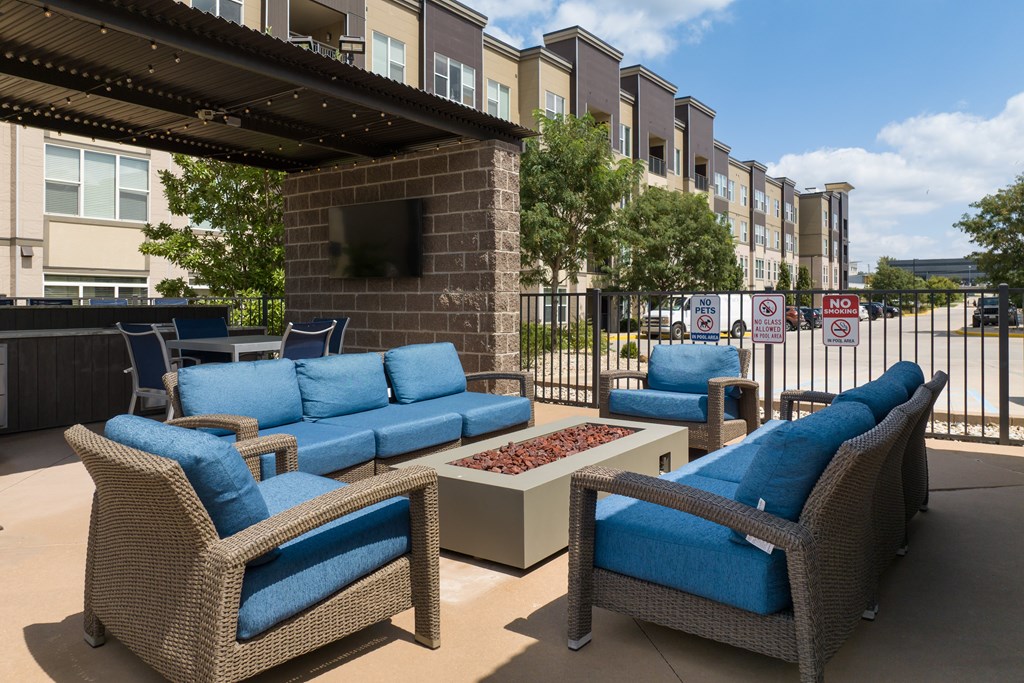 A patio with blue cushioned furniture and a brick fireplace at Alinea Town and Country Luxury Apartments in Des Peres MO 63131..