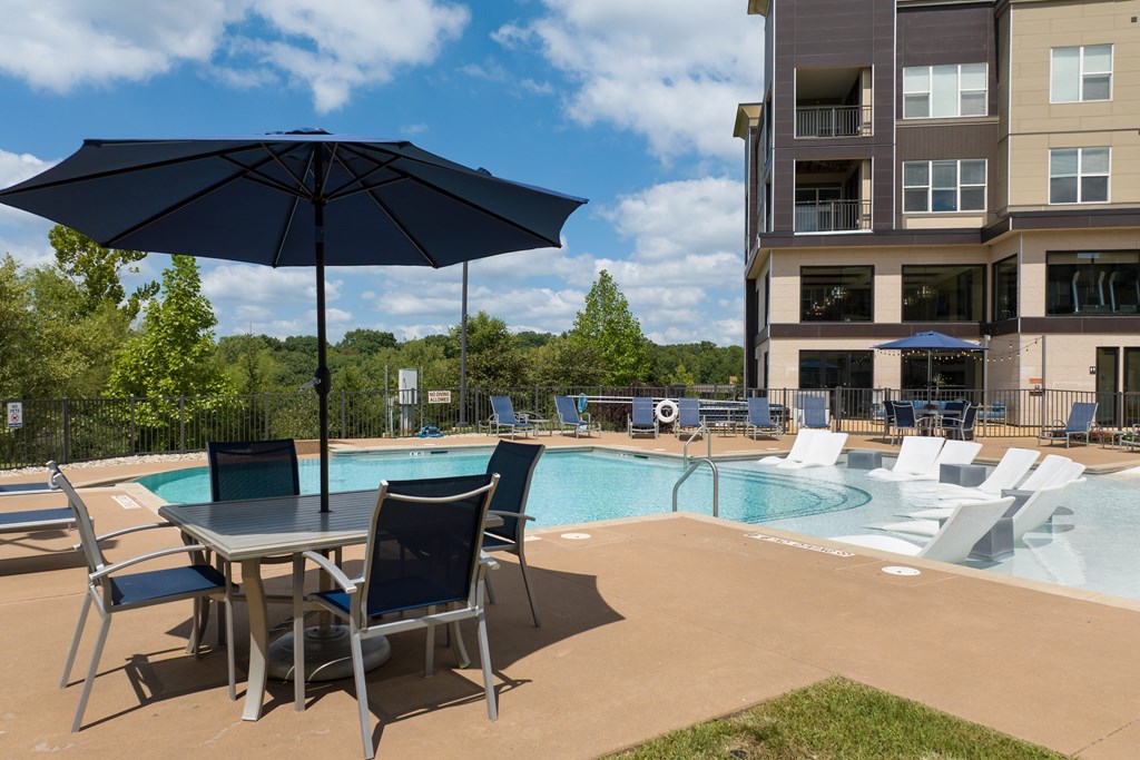 A table with chairs and an umbrella is in front of a poo at Alinea Town and Country Luxury Apartments in Des Peres MO 63131.l.