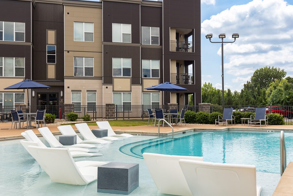 A large swimming pool with lounge chairs and umbrellas in front of a multi-story apartment building. at Alinea Town and Country Luxury Apartments in Des Peres MO 63131.