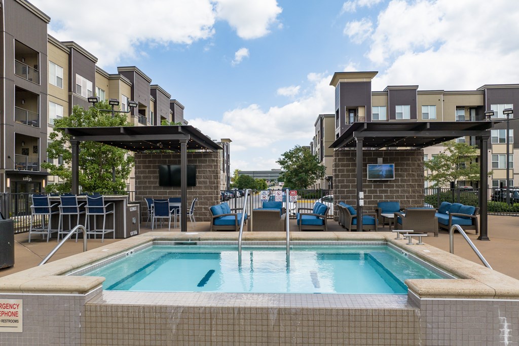 A pool area with a hot tub and lounge chairs in front of apartment buildings at Alinea Town and Country Luxury Apartments in Des Peres MO 63131..