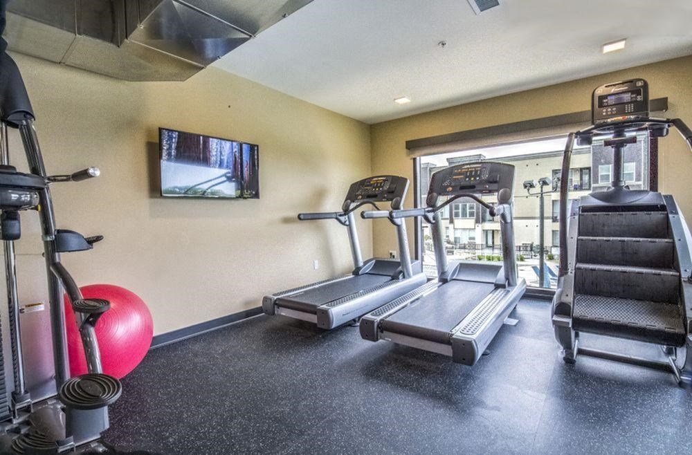 a gym with cardio equipment and a tv on the wall at Alinea Town and Country Luxury Apartments in Des Peres MO 63131.