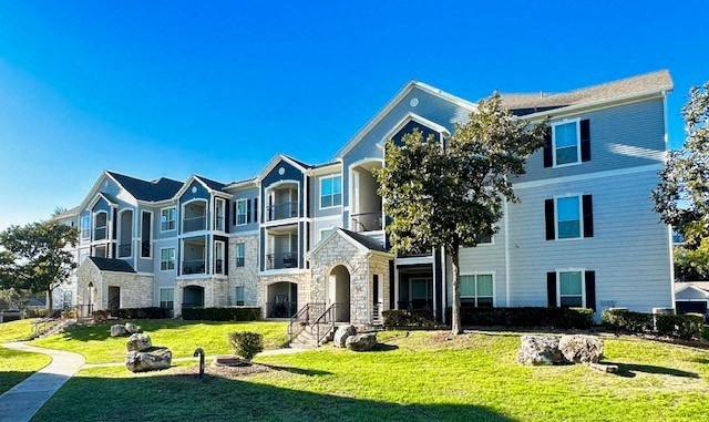 an apartment building with grass and trees in front of it
