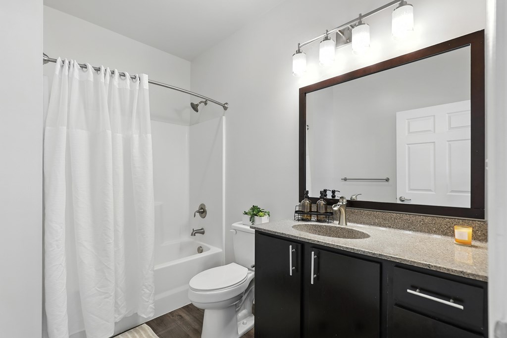 A bathroom with a white toilet, a sink, and a mirror at Bramblett Hills Luxury Apartments in O Fallon MO 63366