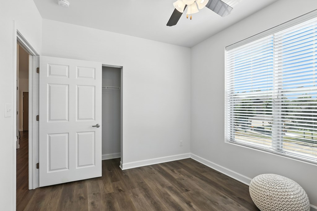 A room with a white door, a window with blinds, and a ceiling fan at Bramblett Hills Luxury Apartments in O Fallon MO 63366