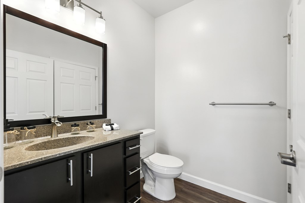A white toilet sits in a bathroom with a sink and mirror at Bramblett Hills Luxury Apartments in O Fallon MO 63366