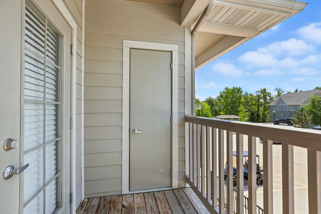A white door is on the left of a balcony with a wooden floor at Bramblett Hills Luxury Apartments in O Fallon MO 63366