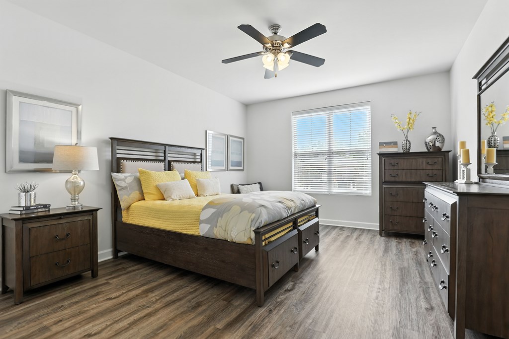 A bedroom with a bed, dresser, and nightstand at Bramblett Hills Luxury Apartments in O Fallon MO 63366
