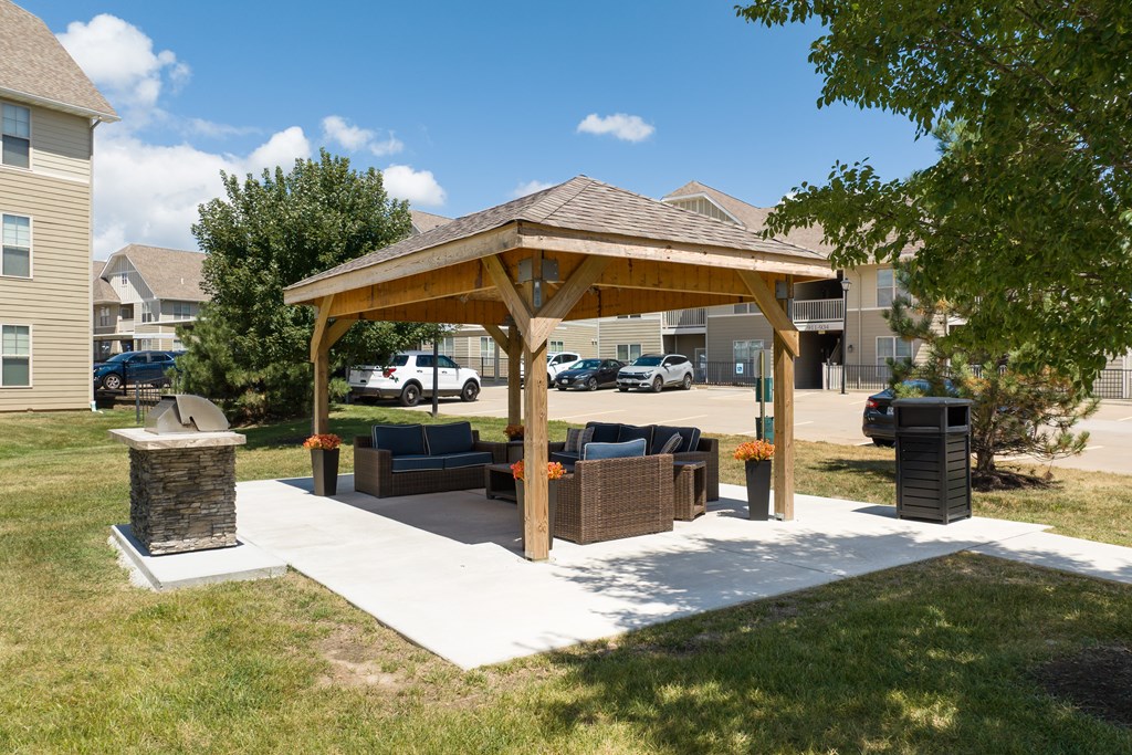 A wooden pavilion with a stone pillar and a bench in front of a building at Bramblett Hills Luxury Apartments in O Fallon MO 63366