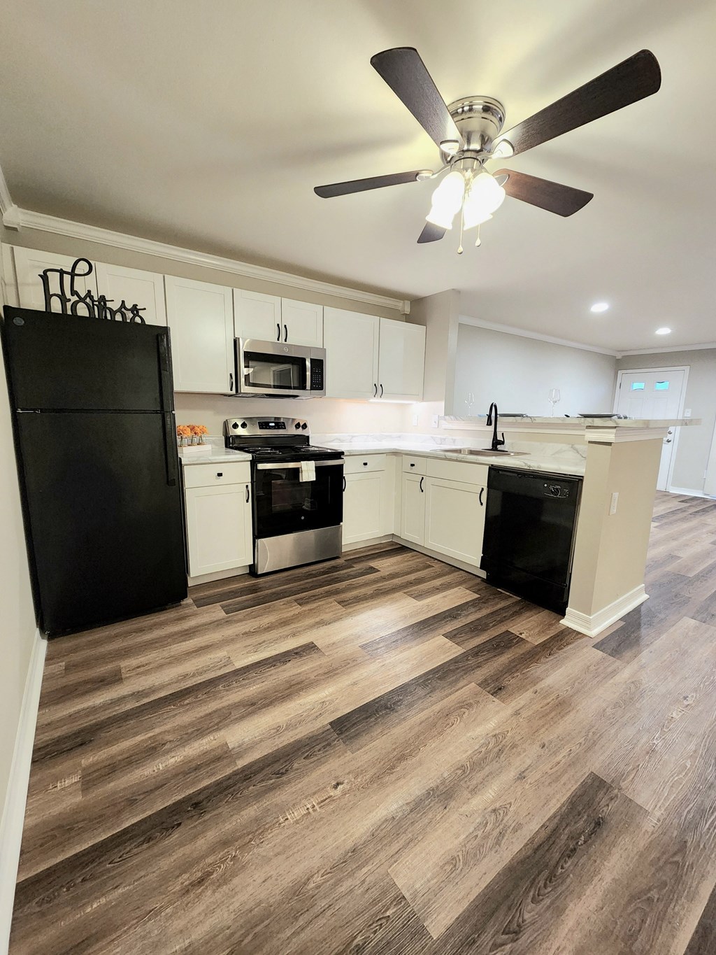 a kitchen with white cabinets and black appliances and a ceiling fan