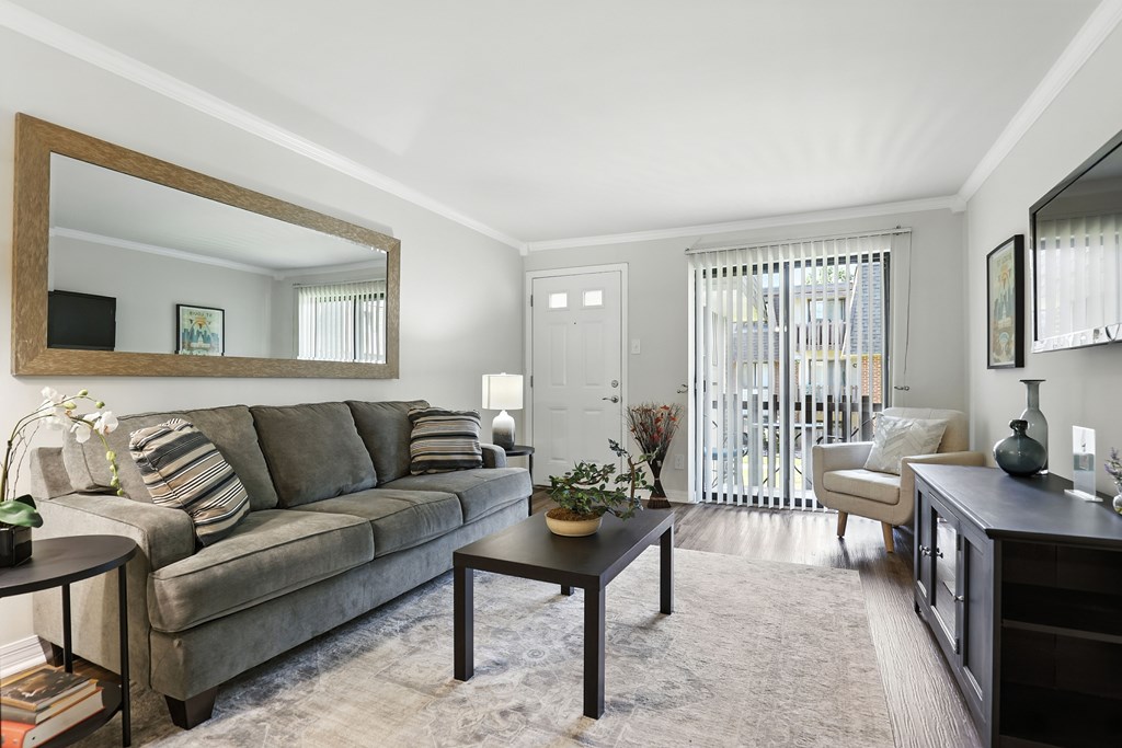 A living room with a grey couch and a large mirror on the wall.