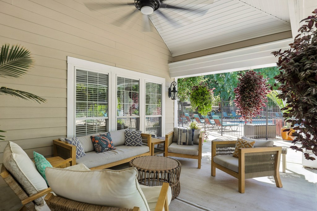 A patio with a white ceiling fan and a white couch with a green pillow.