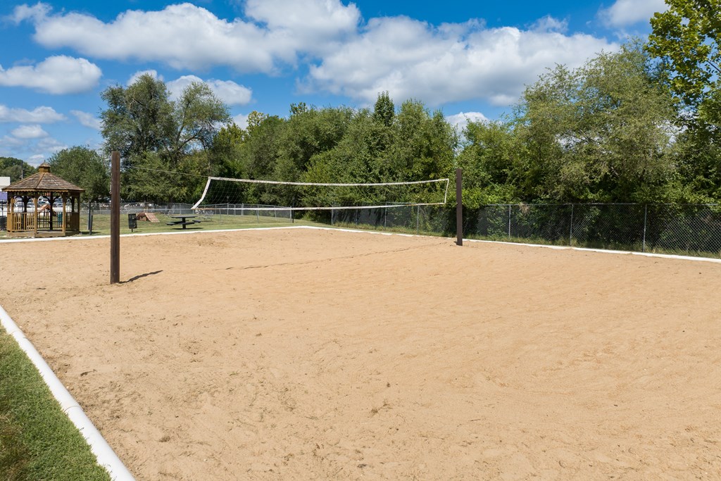 A sandy tennis court surrounded by a fence and trees.