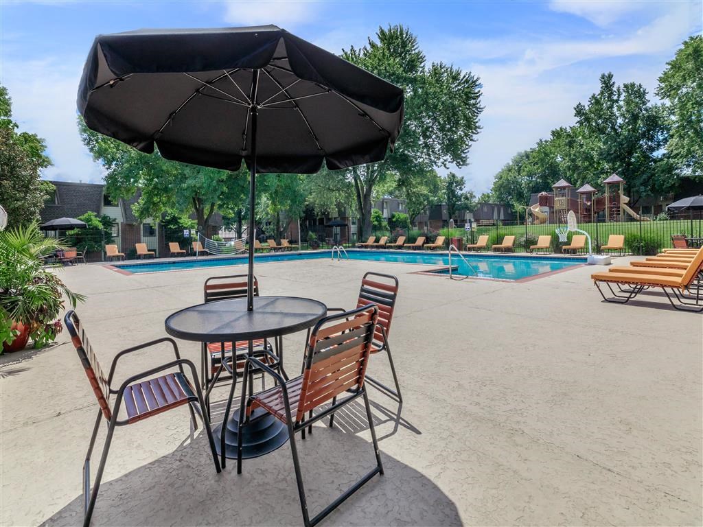 a table with chairs and an umbrella next to a pool