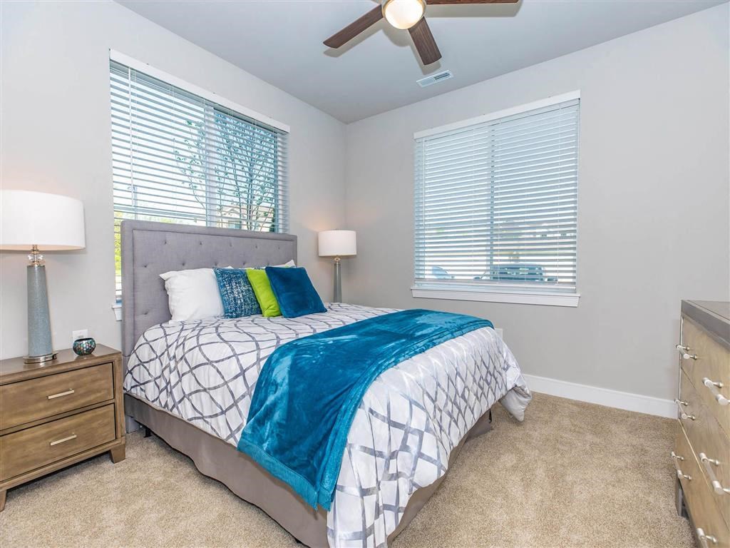 a bedroom with a bed and a ceiling fan and two windows