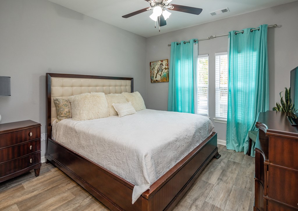 A bedroom with a large bed, a ceiling fan, and a dresser.