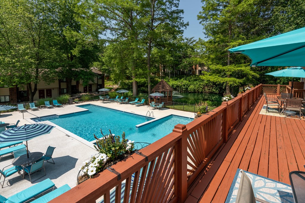 a large swimming pool with a deck with chairs and umbrellas