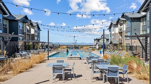 A pool area with chairs and tables is surrounded by apartment buildings.