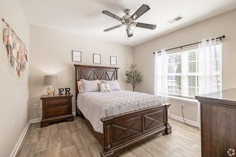 A bedroom with a large bed, a wooden dresser, and a ceiling fan.