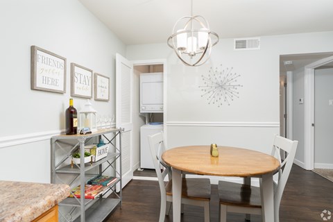 A kitchen with a table and chairs and a shelf with books and a bottle.