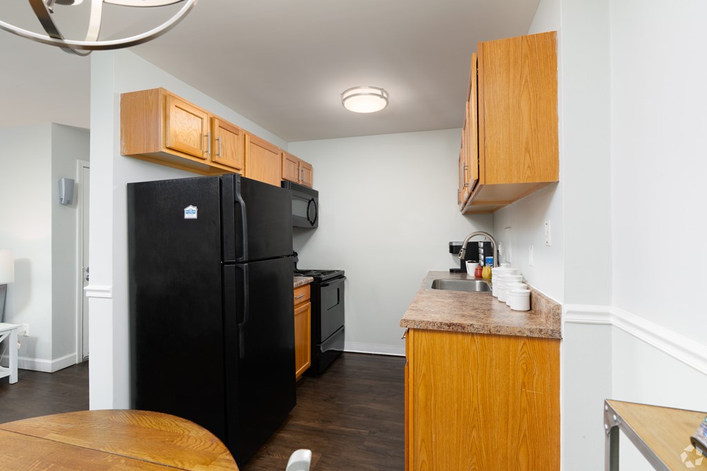 A black refrigerator and microwave in a kitchen with wooden cabinets.