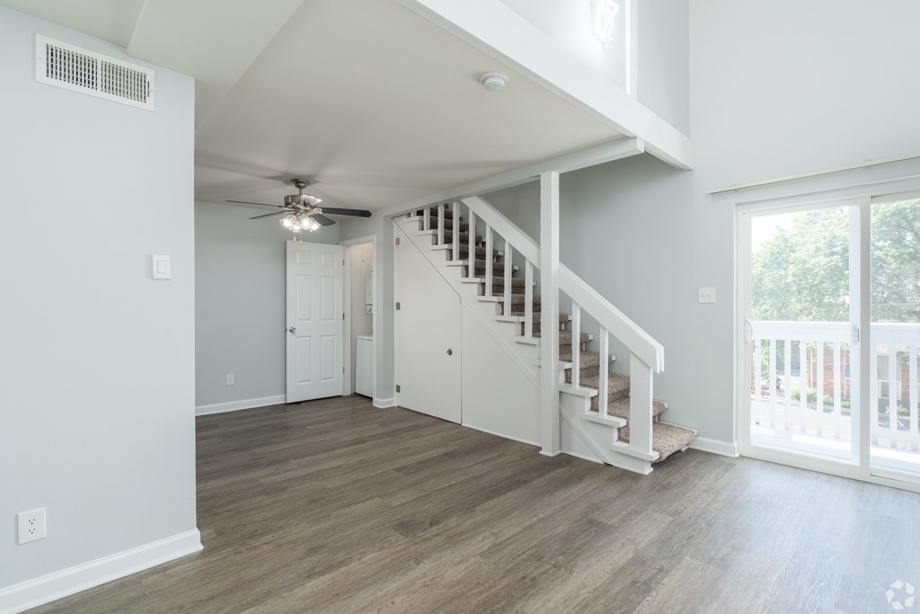 A spacious room with a staircase and a ceiling fan.