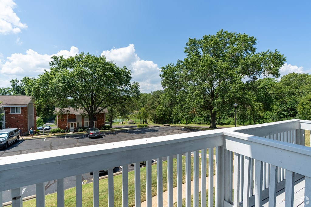 A white railing overlooks a grassy area with trees and a building in the distance.