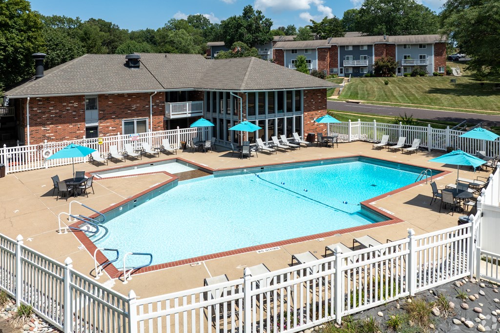 A white fence surrounds a pool with a building in the background.