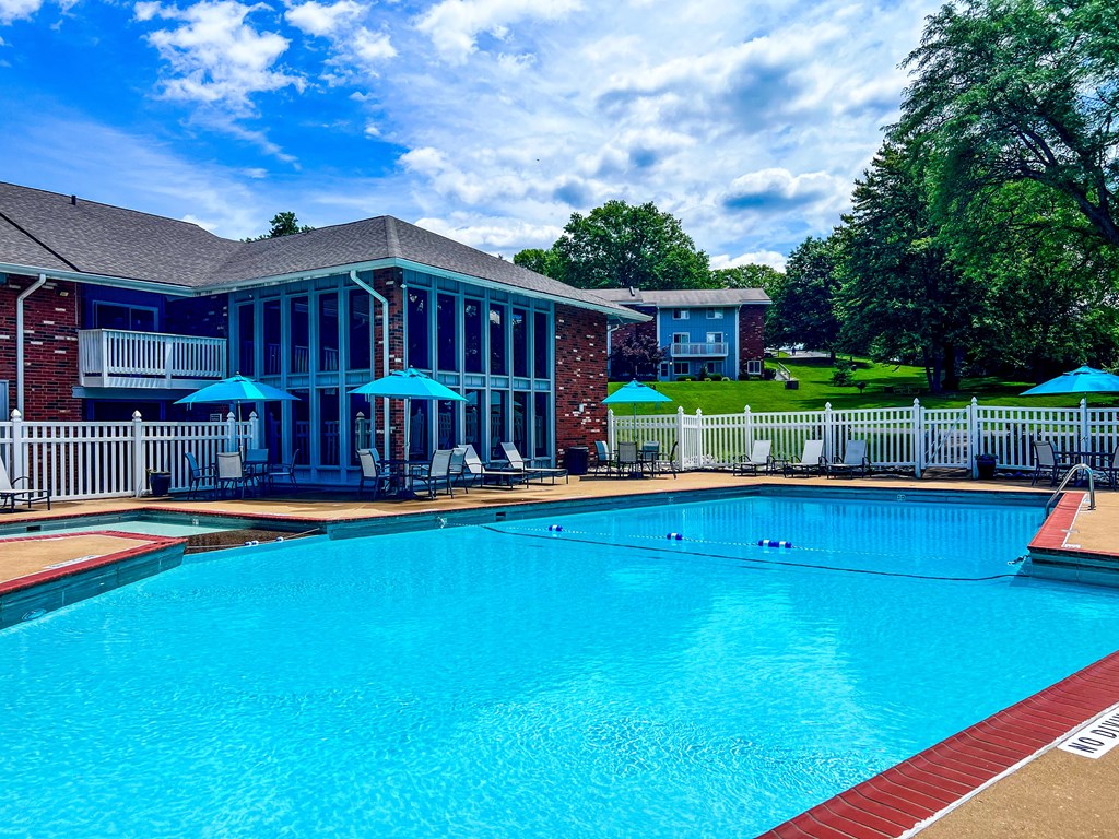 A large swimming pool in front of a house with a deck and umbrellas.