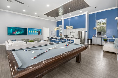 A pool table is in the middle of a room with a kitchen in the background.