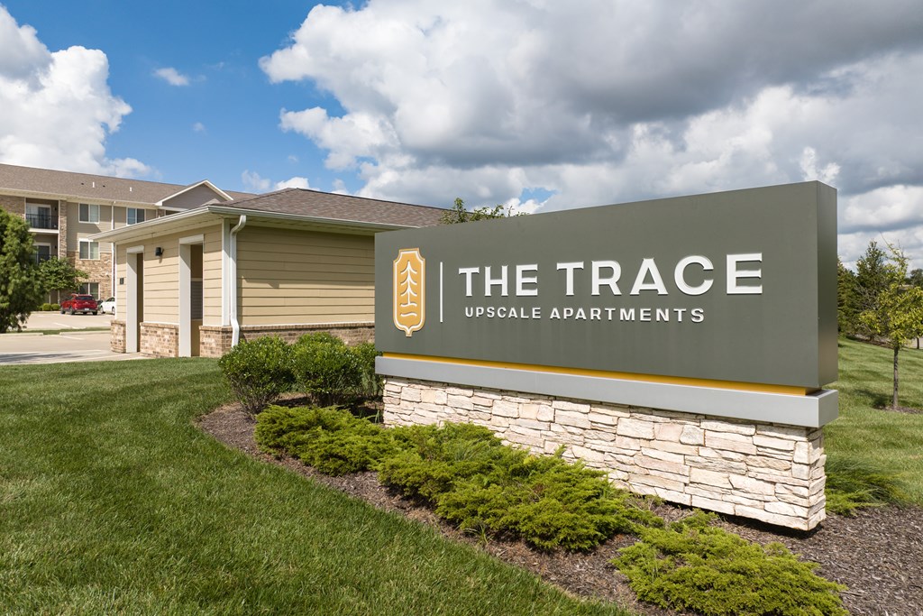 A sign for The Trace Upscale Apartments in front of a building.