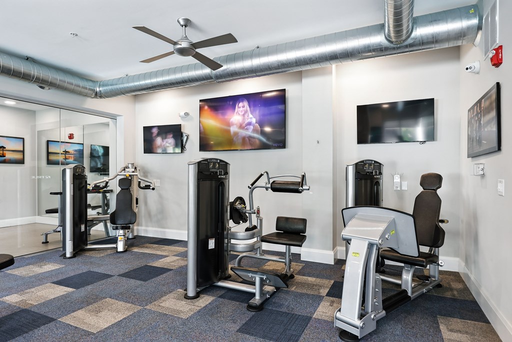 A gym with a variety of equipment including a weight machine, a rowing machine, and a bench press.