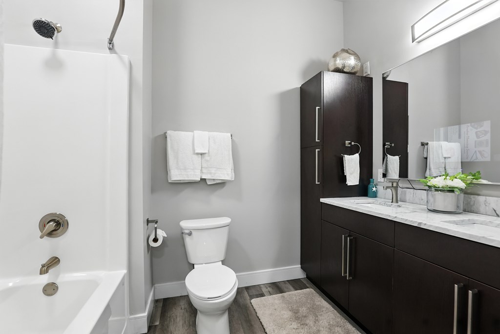 A white toilet sits in a bathroom with a white tub and a sink with a mirror.