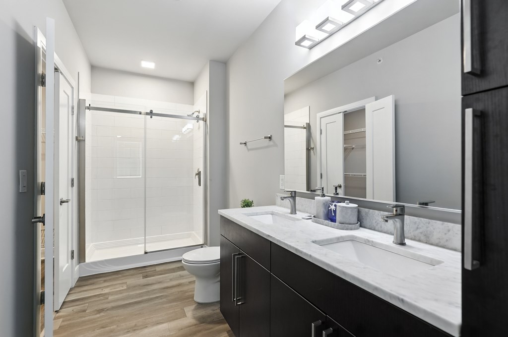 A bathroom with a toilet, sink, mirror, and shower.