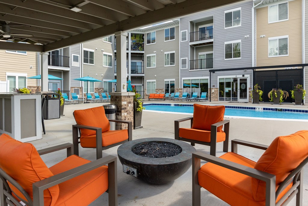 A patio with orange chairs and a fire pit.