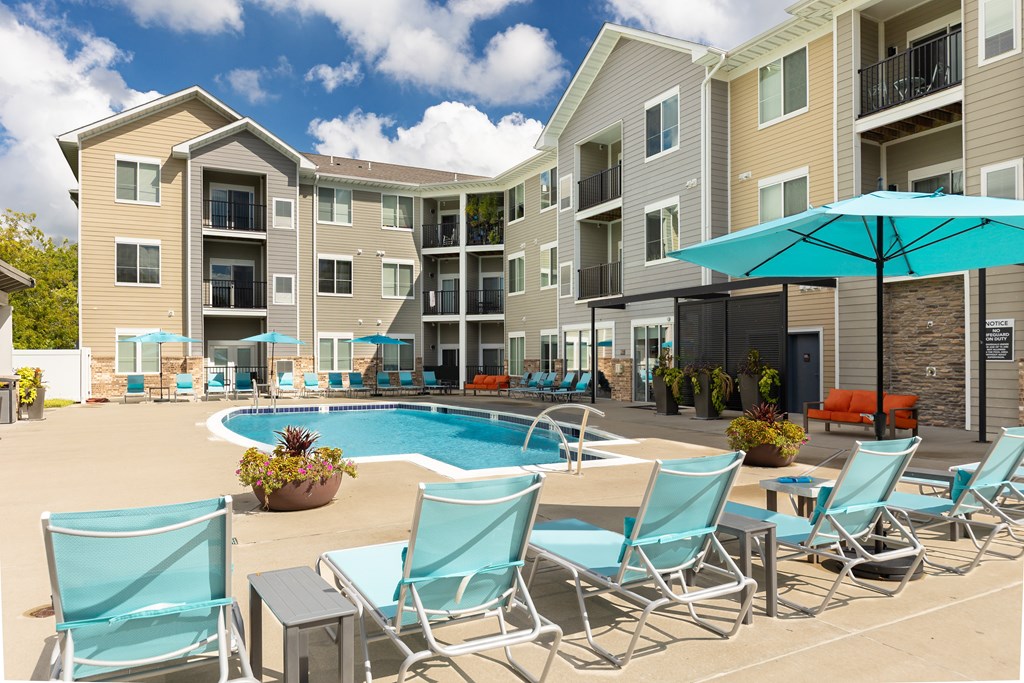 A pool area with chairs and umbrellas in front of apartment buildings.