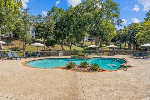 A sparkling pool surrounded by trees and chairs.