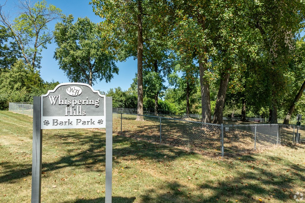 A sign for Whispering Hills Bark Park stands in a grassy area.