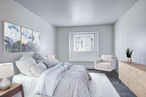 A bedroom with a large bed, a white chair, and a painting on the wall.