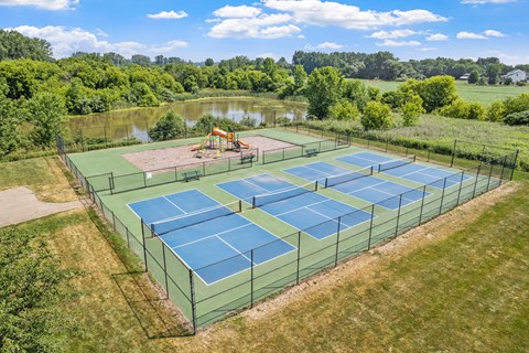 A tennis court surrounded by a green fence with a playground in the background.