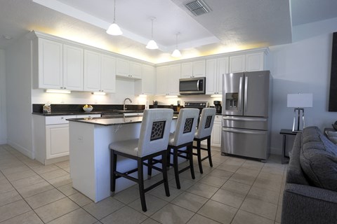 a kitchen with an island with chairs and a sink and a refrigerator
