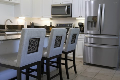 a kitchen with a center island with three white chairs and a stainless steel refrigerator