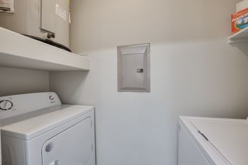 A white washing machine sits next to a white dryer in a small laundry room.