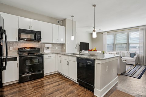 A modern kitchen with white cabinets and black appliances.