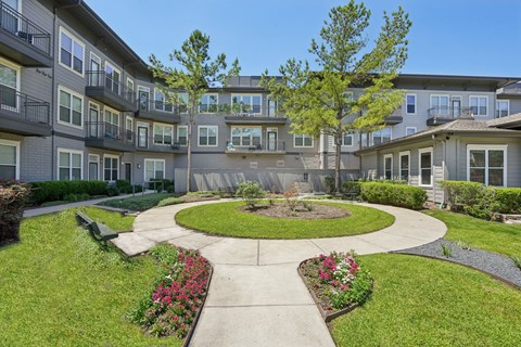 A courtyard with a circular walkway and a bench is surrounded by apartment buildings.