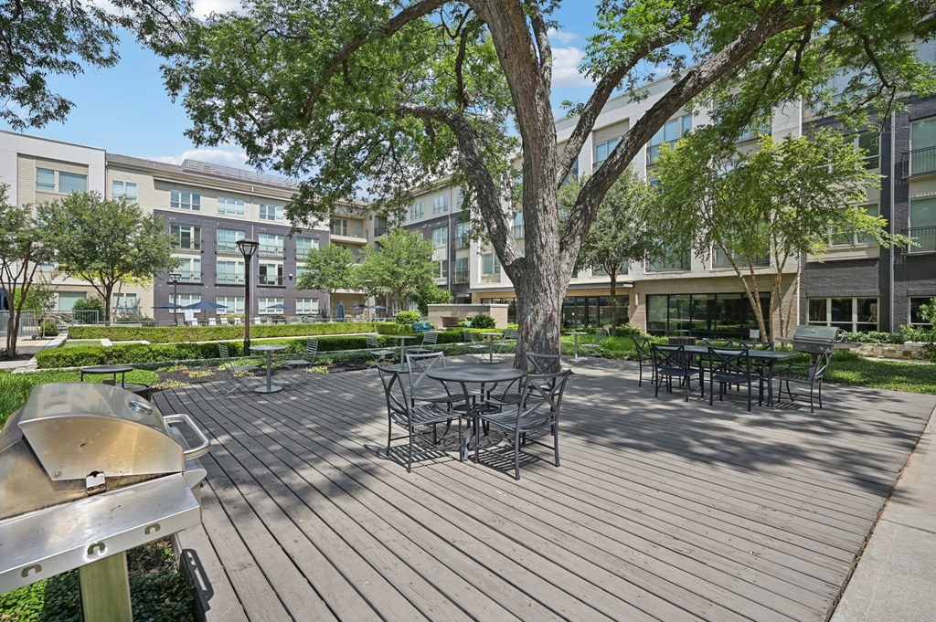 A wooden deck with a grill and chairs is surrounded by trees at Everra Midtown Park Apartments, Dallas, TX